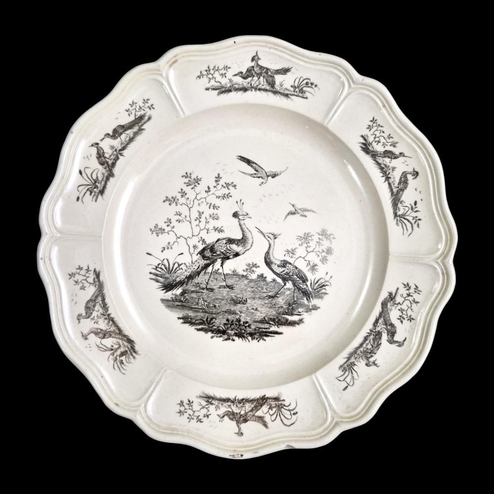 A pair of round cream-coloured earthenware plates featuring monochrome transfer prints of birds and moulded scalloped rims. View VI