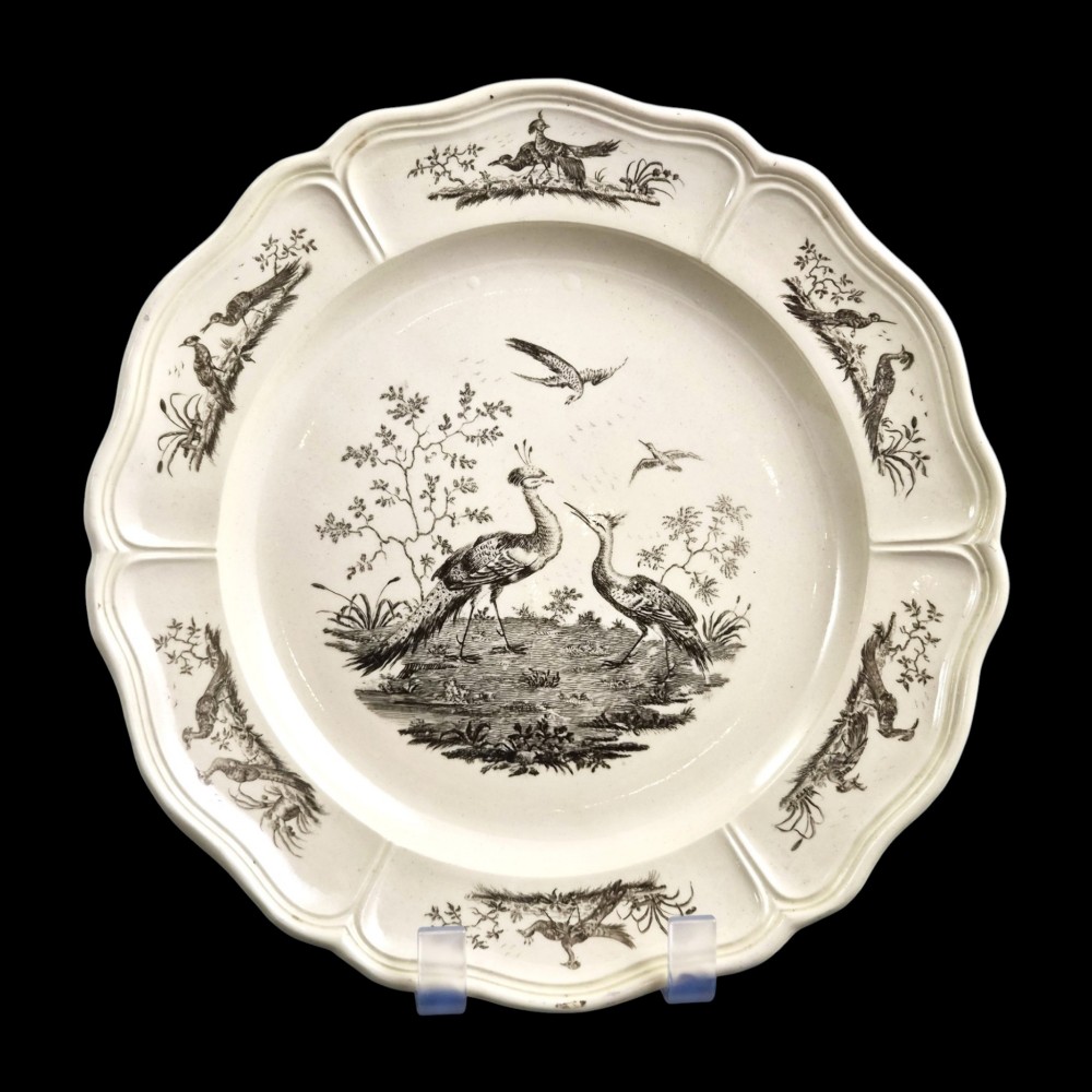 A pair of round cream-coloured earthenware plates featuring monochrome transfer prints of birds and moulded scalloped rims. View XII