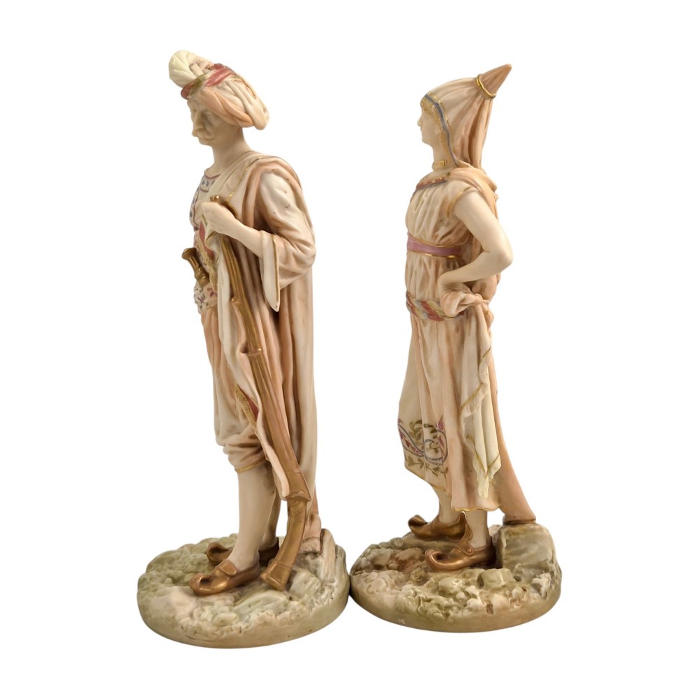 A pair of late Victorian Royal Worcester blush ivory porcelain figures depicting an Indian man and woman in detailed traditional attire with gilded accents. View II