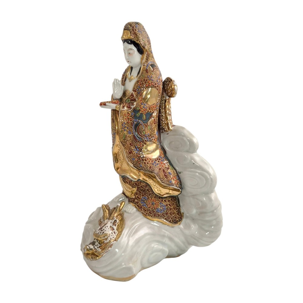 A Japanese Kutani porcelain figure of the deity Kannon in detailed patterned robes, standing atop a white sea dragon amidst sculpted waves. View III