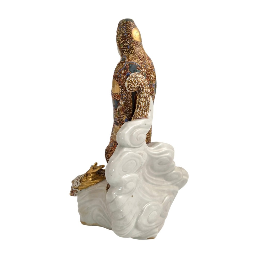 A Japanese Kutani porcelain figure of the deity Kannon in detailed patterned robes, standing atop a white sea dragon amidst sculpted waves. View IV