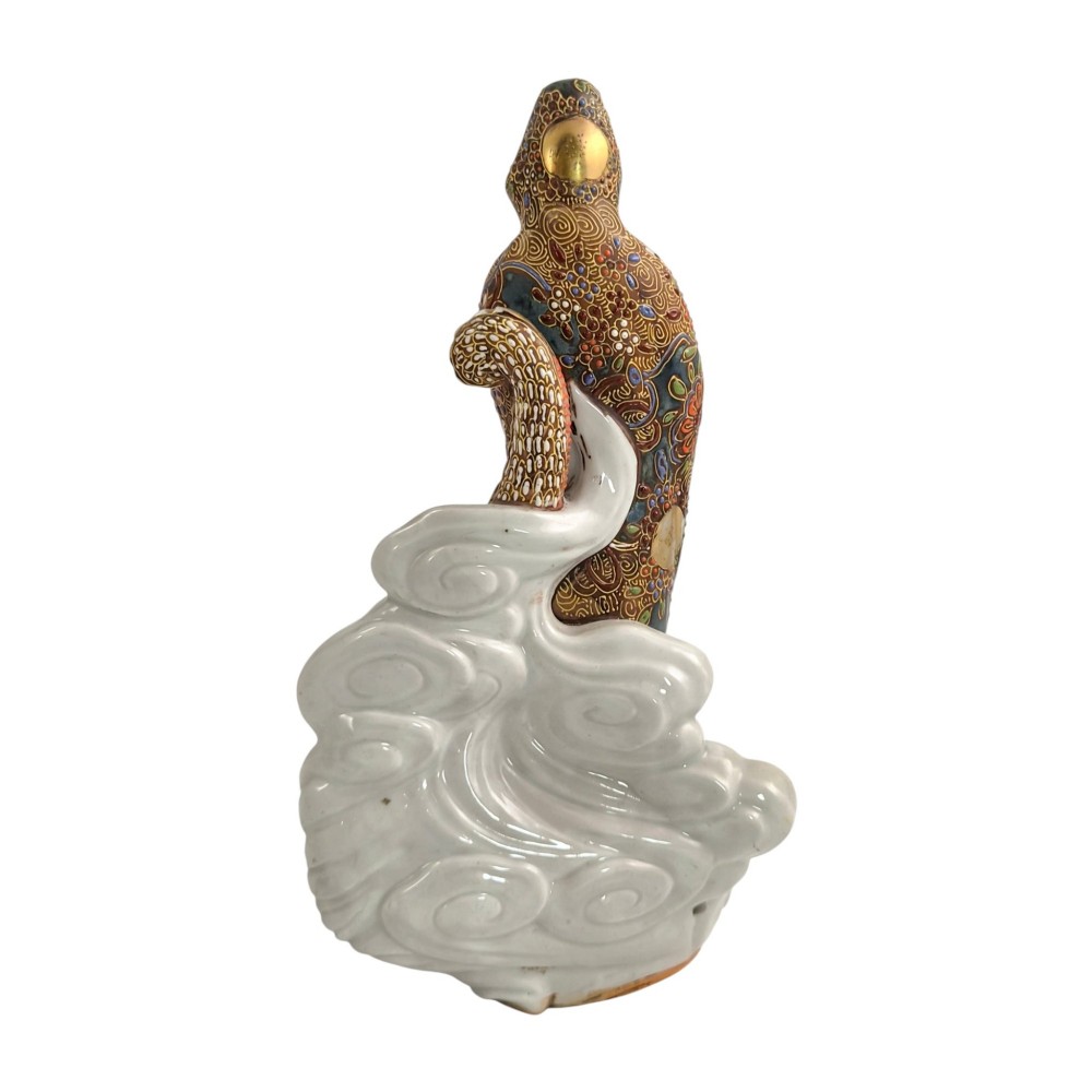A Japanese Kutani porcelain figure of the deity Kannon in detailed patterned robes, standing atop a white sea dragon amidst sculpted waves. View V