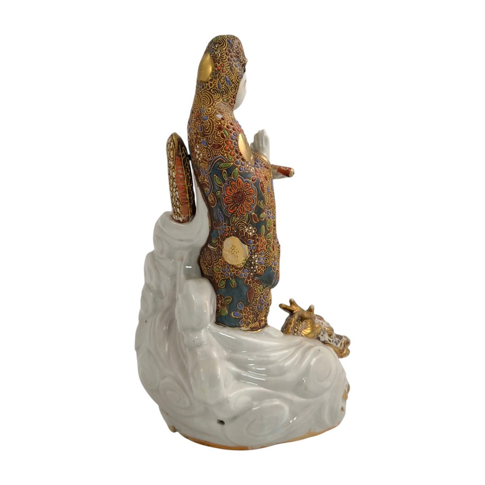 A Japanese Kutani porcelain figure of the deity Kannon in detailed patterned robes, standing atop a white sea dragon amidst sculpted waves. View VI