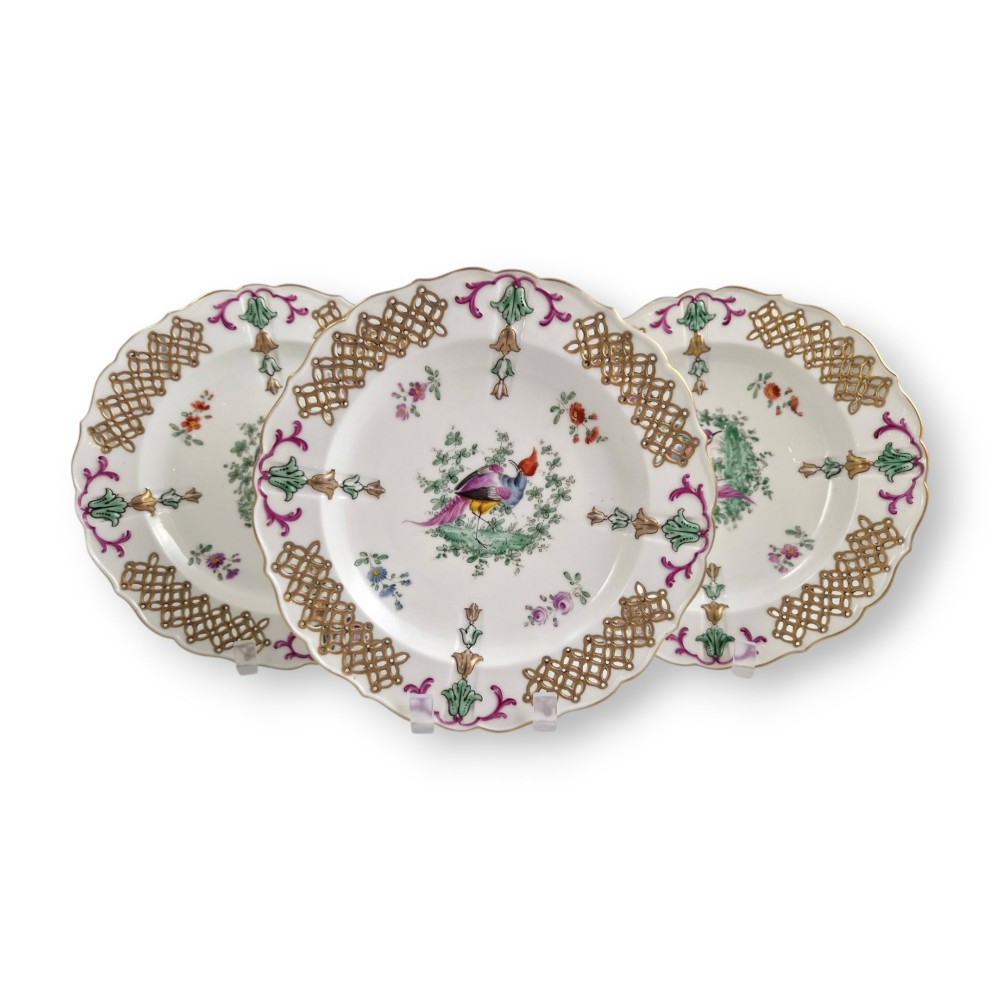 Set of three white porcelain cabinet plates featuring pierced lattice rims decorated with gold gilding, pink scrolls, green accents, and hand-painted exotic birds in the centre.