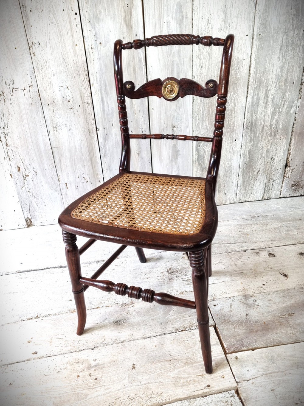 A Regency period side chair featuring a simulated rosewood finish, a rope-twist top rail, a brass-mounted centre splat, turned legs, and a hand-woven cane seat.