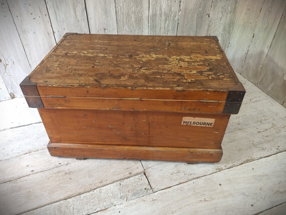 A late Victorian pine travel trunk featuring a distressed wood lid, painted sides with vintage shipping labels, central keyhole, and metal corner reinforcements. View III