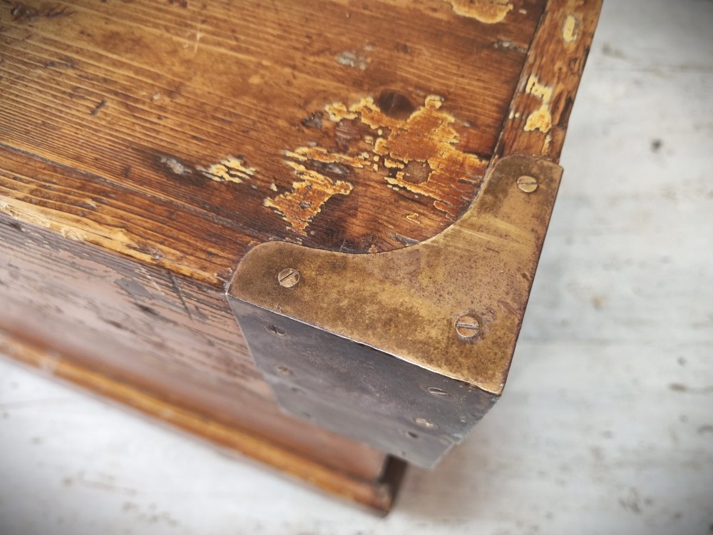 A late Victorian pine travel trunk featuring a distressed wood lid, painted sides with vintage shipping labels, central keyhole, and metal corner reinforcements. View V
