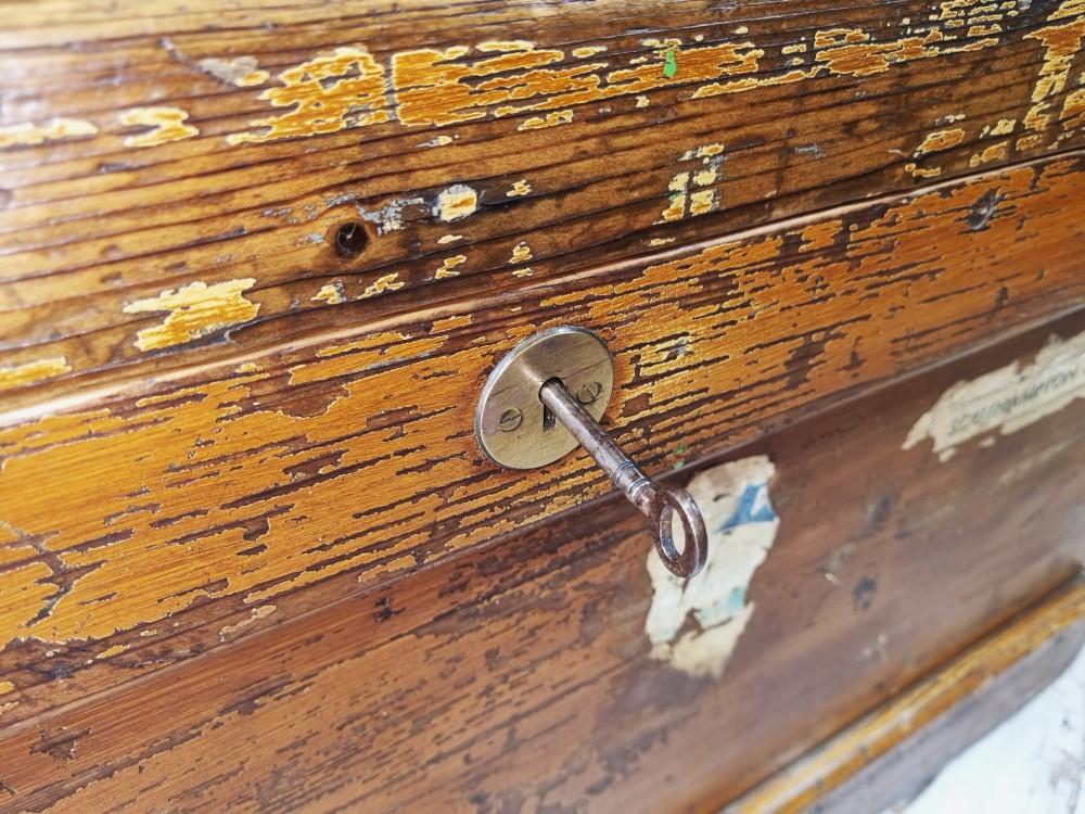 A late Victorian pine travel trunk featuring a distressed wood lid, painted sides with vintage shipping labels, central keyhole, and metal corner reinforcements. View VI