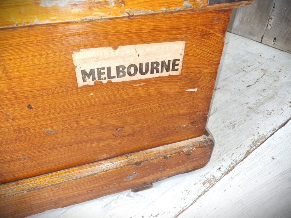 A late Victorian pine travel trunk featuring a distressed wood lid, painted sides with vintage shipping labels, central keyhole, and metal corner reinforcements. View VII