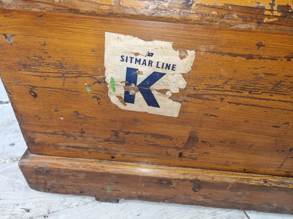 A late Victorian pine travel trunk featuring a distressed wood lid, painted sides with vintage shipping labels, central keyhole, and metal corner reinforcements. View VIII