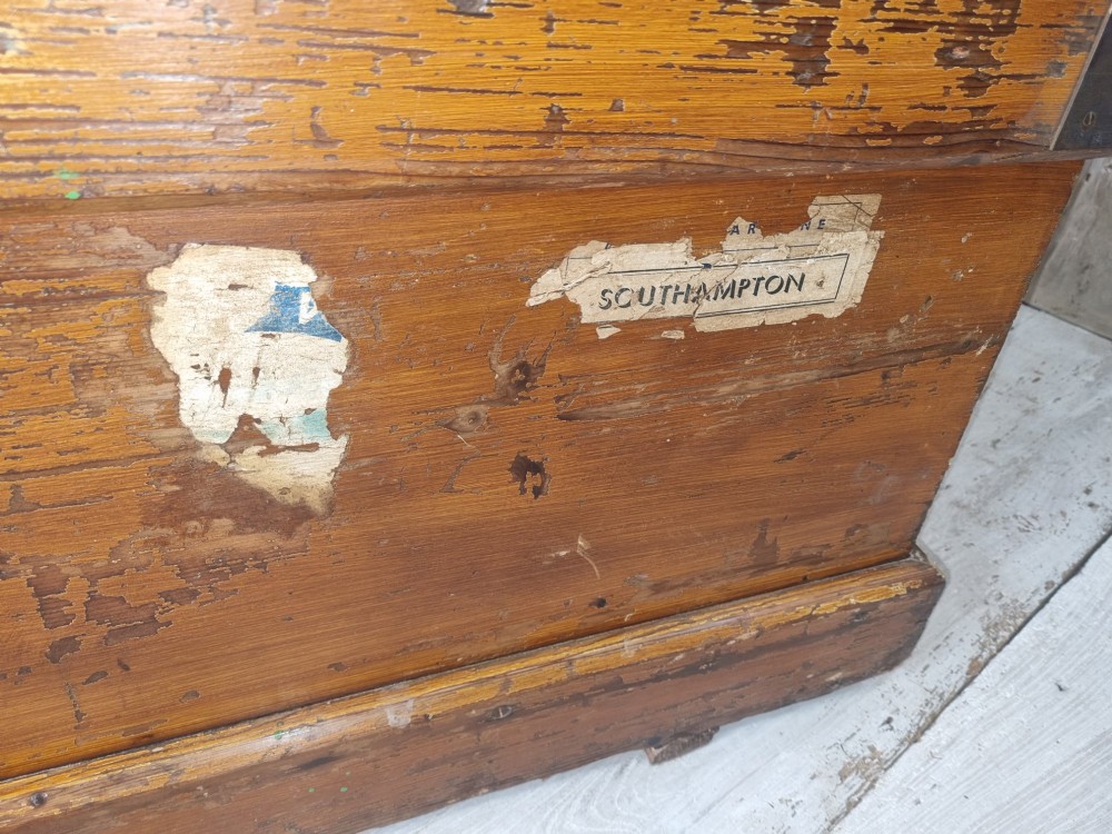 A late Victorian pine travel trunk featuring a distressed wood lid, painted sides with vintage shipping labels, central keyhole, and metal corner reinforcements. View IX