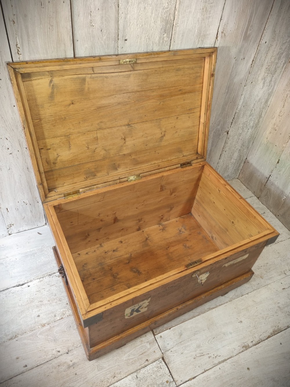 A late Victorian pine travel trunk featuring a distressed wood lid, painted sides with vintage shipping labels, central keyhole, and metal corner reinforcements. View XI