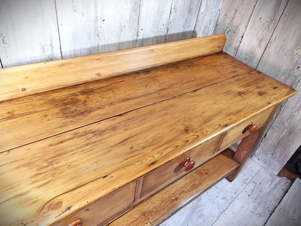 A Victorian pine dresser base featuring three upper drawers with turned wooden knobs, a simple rear upstand, and an open lower pot shelf. View VI