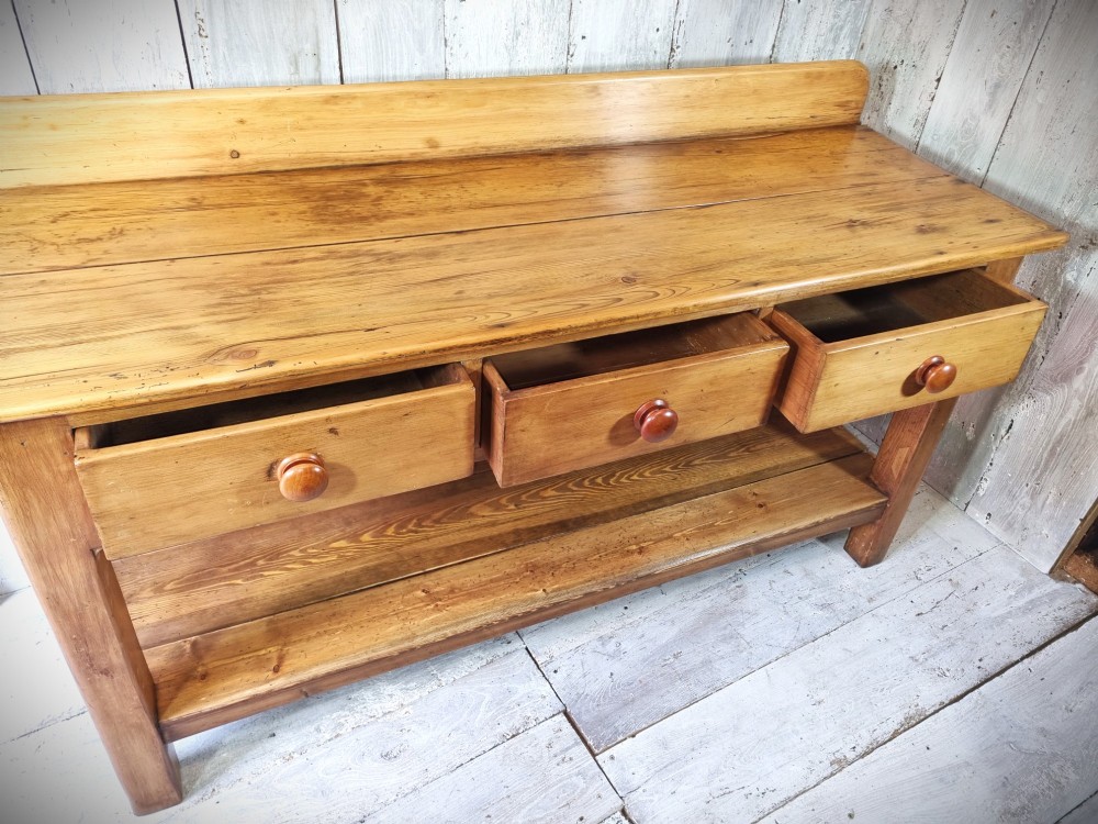 A Victorian pine dresser base featuring three upper drawers with turned wooden knobs, a simple rear upstand, and an open lower pot shelf. View VII