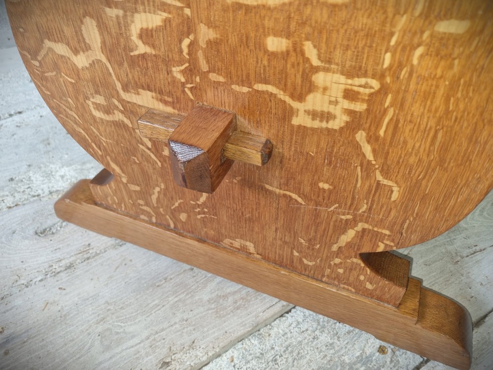 A solid golden oak trestle table featuring a rectangular top, shaped side supports with visible medullary ray grain patterns, and a central stretcher secured with pegged tenons. View VI