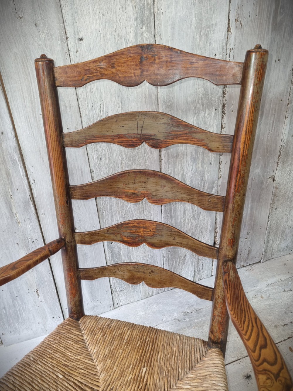 An antique Cheshire ladder back armchair featuring shaped horizontal slats, swept armrests, turned legs, and a woven rush seat. View VII
