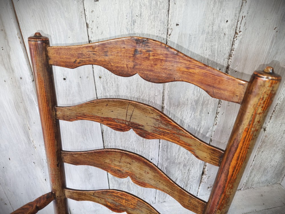 An antique Cheshire ladder back armchair featuring shaped horizontal slats, swept armrests, turned legs, and a woven rush seat. View VIII