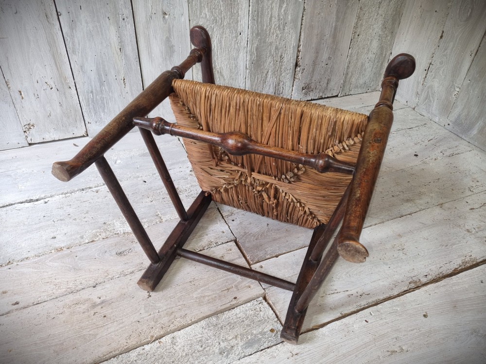 An antique Cheshire ladder back armchair featuring shaped horizontal slats, swept armrests, turned legs, and a woven rush seat. View X