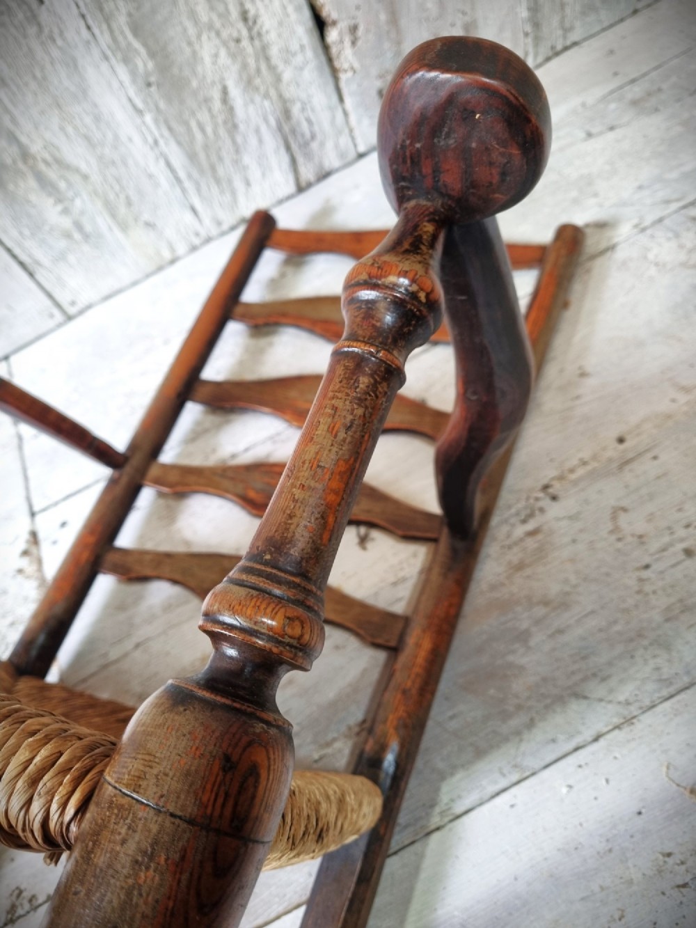 An antique Cheshire ladder back armchair featuring shaped horizontal slats, swept armrests, turned legs, and a woven rush seat. View XI