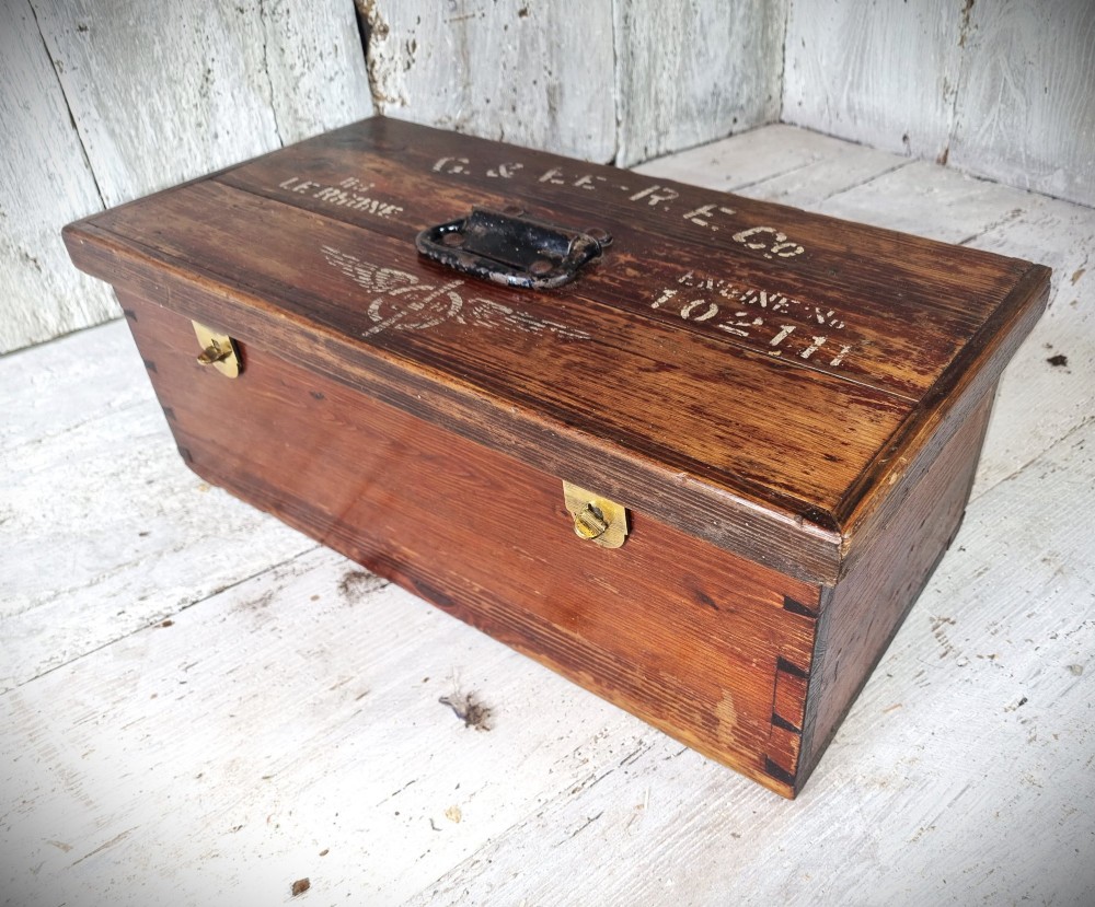 A rectangular warm brown wooden tool box featuring white stencilled text, a central winged logo, and an iron top clasp. View II