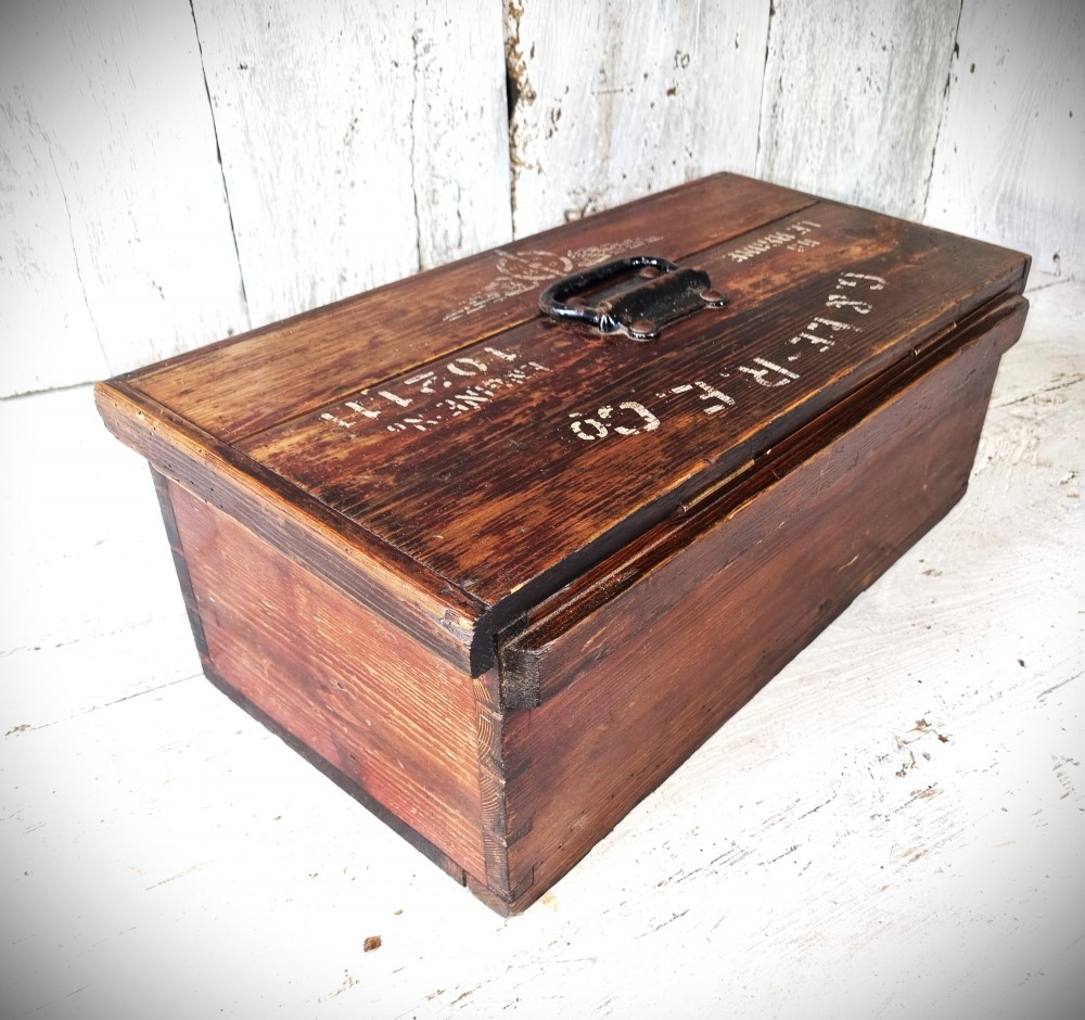 A rectangular warm brown wooden tool box featuring white stencilled text, a central winged logo, and an iron top clasp. View III
