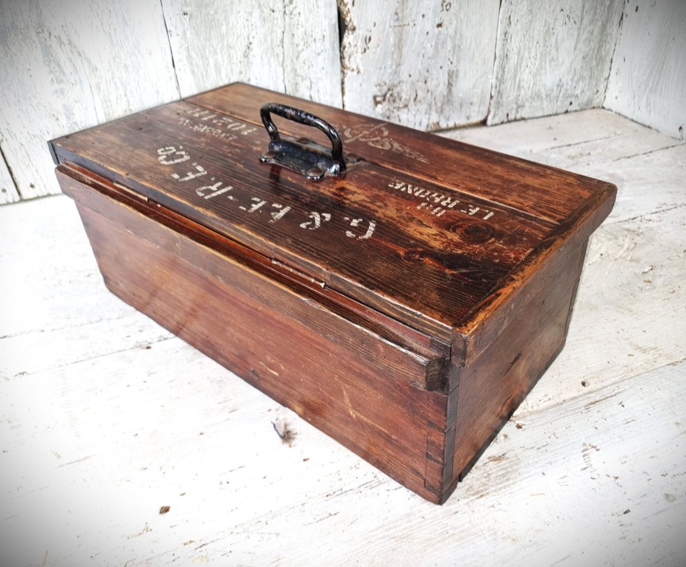A rectangular warm brown wooden tool box featuring white stencilled text, a central winged logo, and an iron top clasp. View IV
