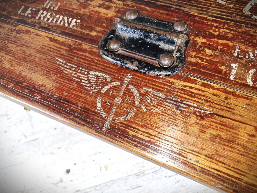 A rectangular warm brown wooden tool box featuring white stencilled text, a central winged logo, and an iron top clasp. View V
