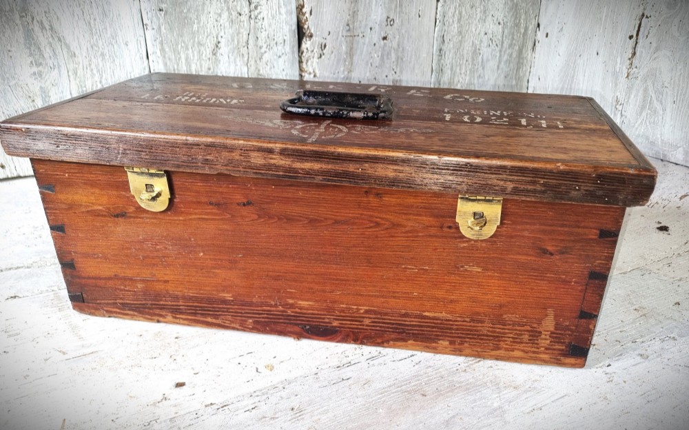 A rectangular warm brown wooden tool box featuring white stencilled text, a central winged logo, and an iron top clasp. View IX