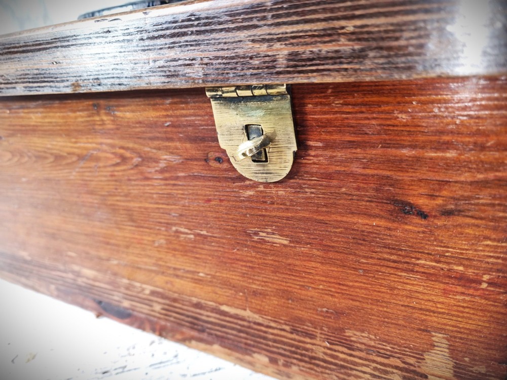 A rectangular warm brown wooden tool box featuring white stencilled text, a central winged logo, and an iron top clasp. View X