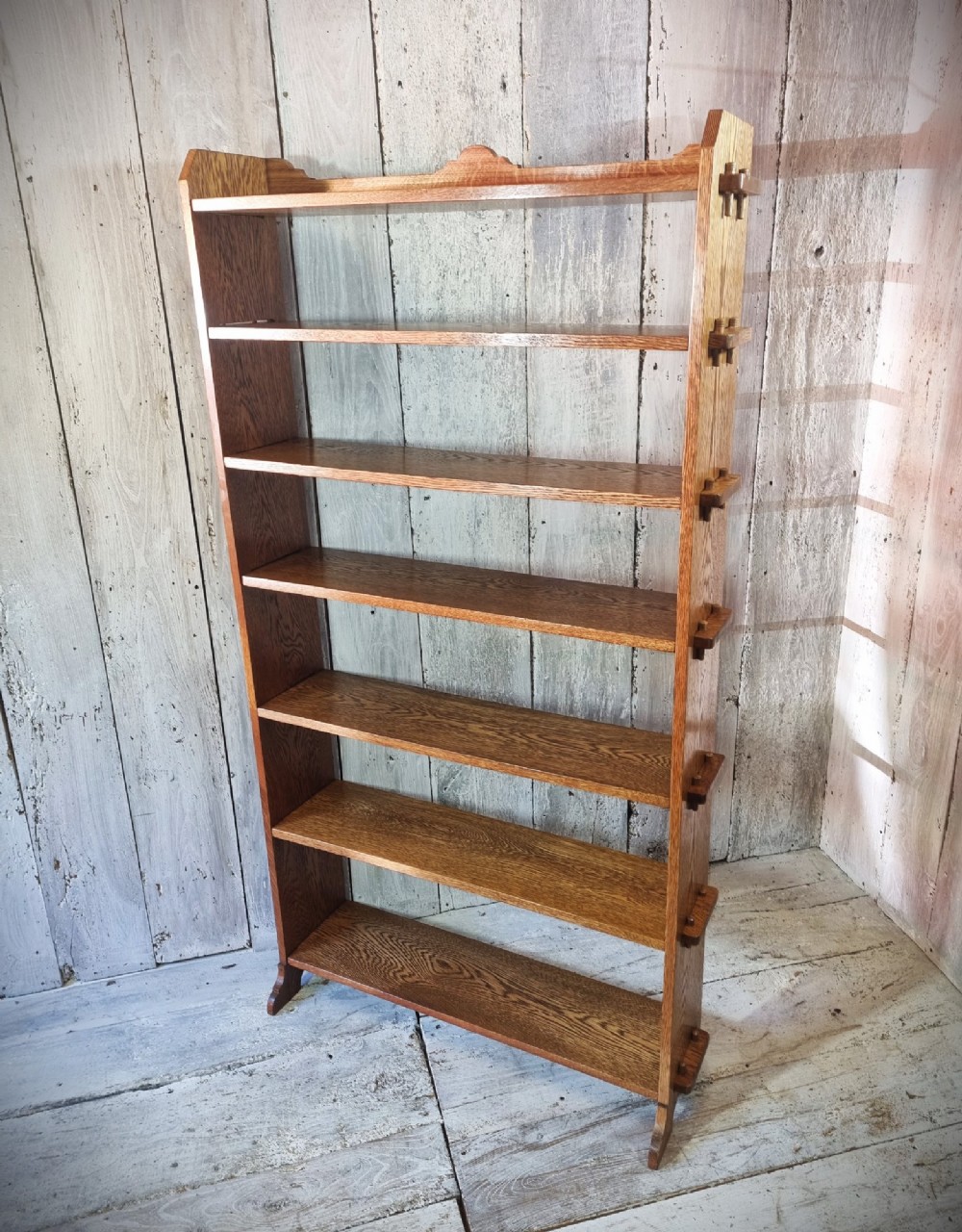 A tall open-backed oak shelving unit featuring seven horizontal tiers and visible side pegged joinery. View X