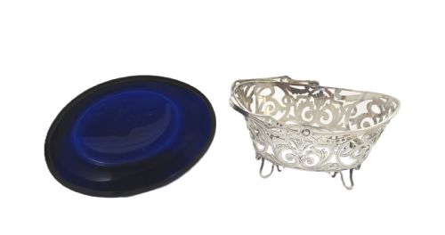 fig 1. An antique Victorian sterling silver basket with intricate scrollwork piercing, an overhead swing handle, four small feet, and a dark cobalt blue glass liner.