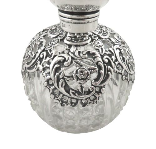 fig 1. An Edwardian clear glass scent bottle featuring a round body with ornate embossed sterling silver overlay and matching cap.