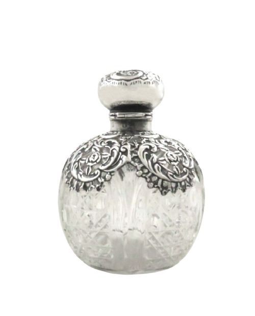 An Edwardian clear glass scent bottle featuring a round body with ornate embossed sterling silver overlay and matching cap. View IX