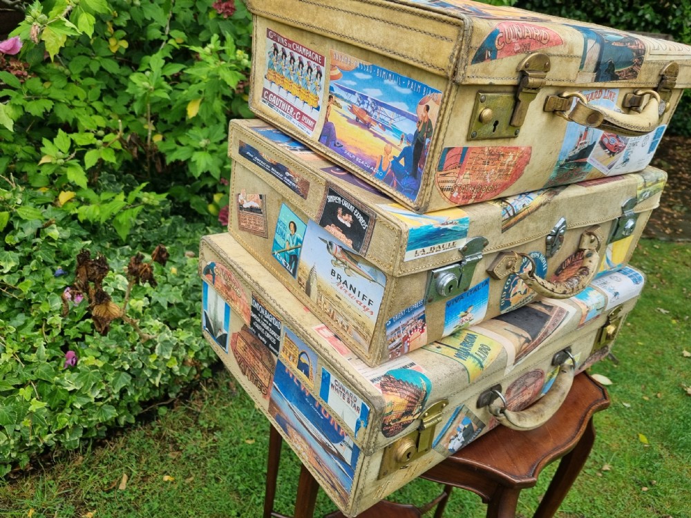 A graduated stack of three cream vellum suitcases covered in colorful travel stickers and fitted with brass latches. View III