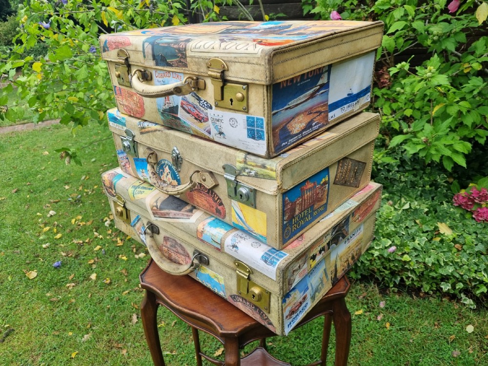 A graduated stack of three cream vellum suitcases covered in colorful travel stickers and fitted with brass latches.