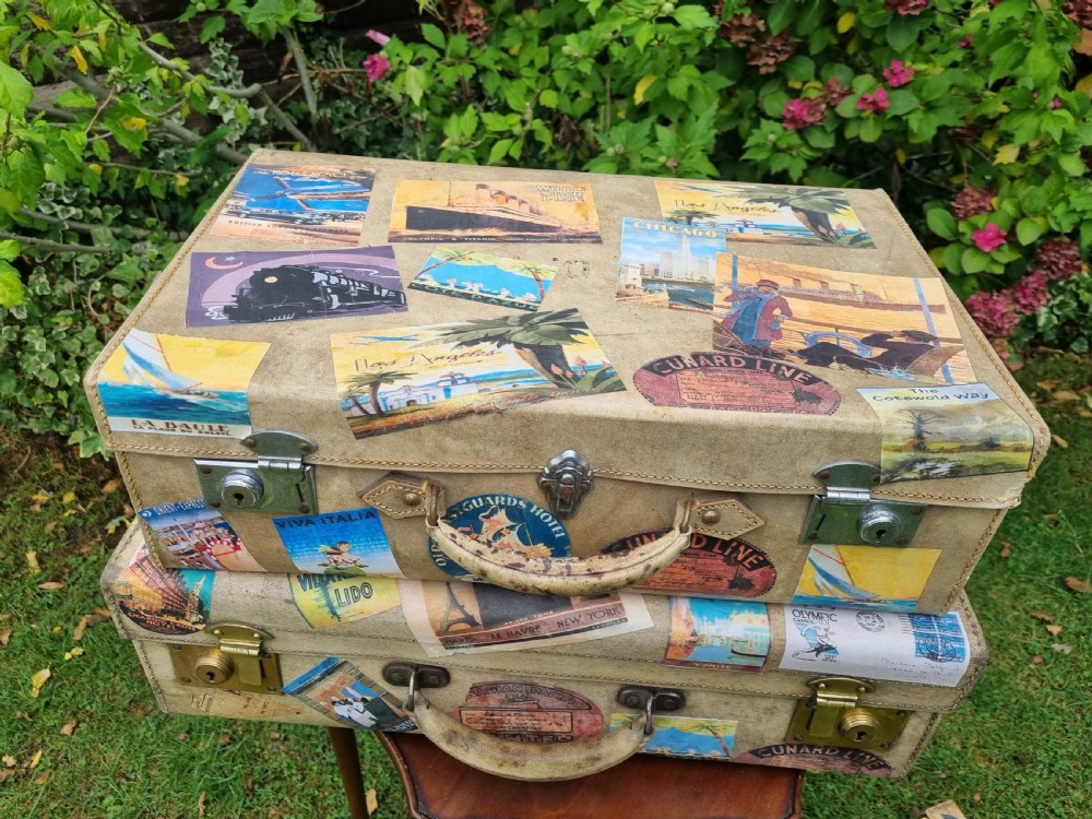 A graduated stack of three cream vellum suitcases covered in colorful travel stickers and fitted with brass latches. View VI