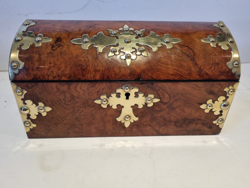 A Victorian burr walnut stationery box with a dome lid, ornamented with pierced brass mounts and a decorative brass keyhole escutcheon.