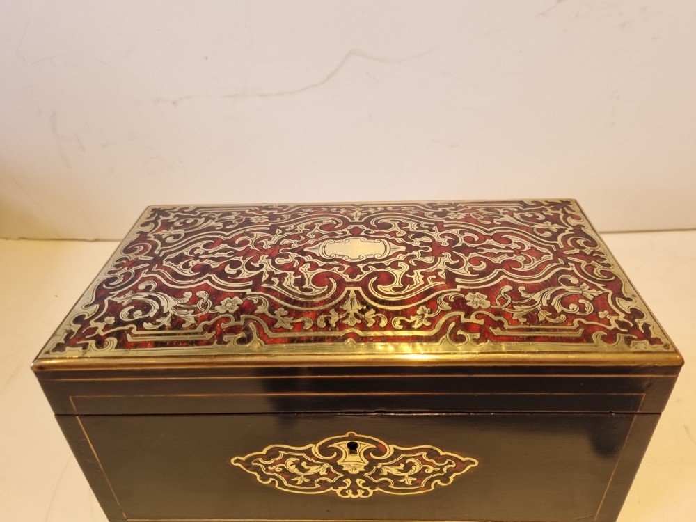 A rectangular ebonised wood tea caddy featuring a lid ornamented with red tortoiseshell and brass Boulle marquetry and a brass-inlaid keyhole escutcheon on the front. View II