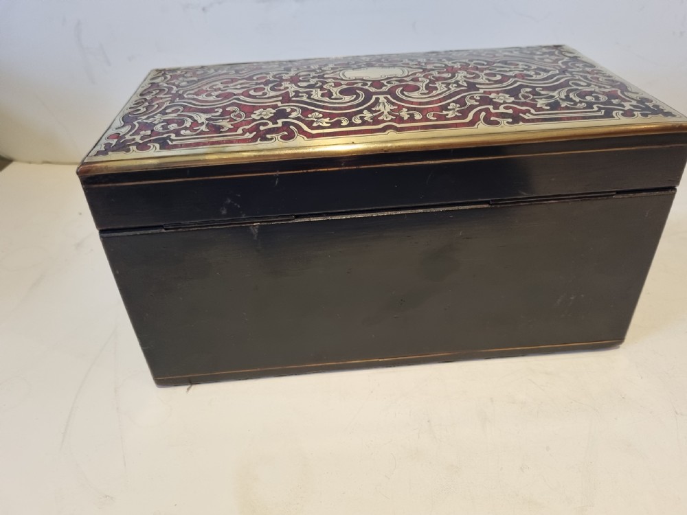 A rectangular ebonised wood tea caddy featuring a lid ornamented with red tortoiseshell and brass Boulle marquetry and a brass-inlaid keyhole escutcheon on the front. View IV