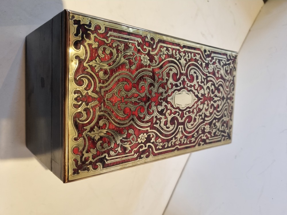 A rectangular ebonised wood tea caddy featuring a lid ornamented with red tortoiseshell and brass Boulle marquetry and a brass-inlaid keyhole escutcheon on the front. View IX