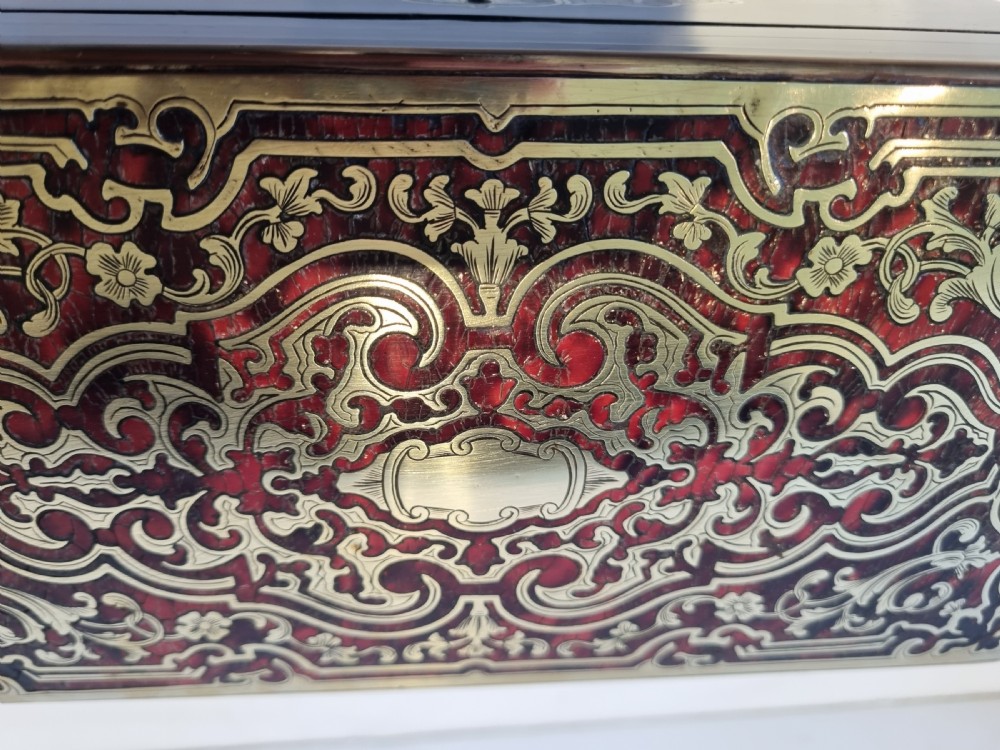 A rectangular ebonised wood tea caddy featuring a lid ornamented with red tortoiseshell and brass Boulle marquetry and a brass-inlaid keyhole escutcheon on the front. View X