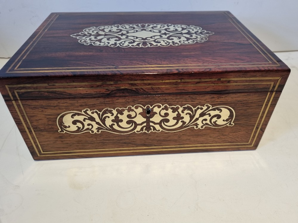 A rectangular dark rosewood box featuring intricate brass floral scrollwork inlay and brass double-stringing on the lid and front panel.