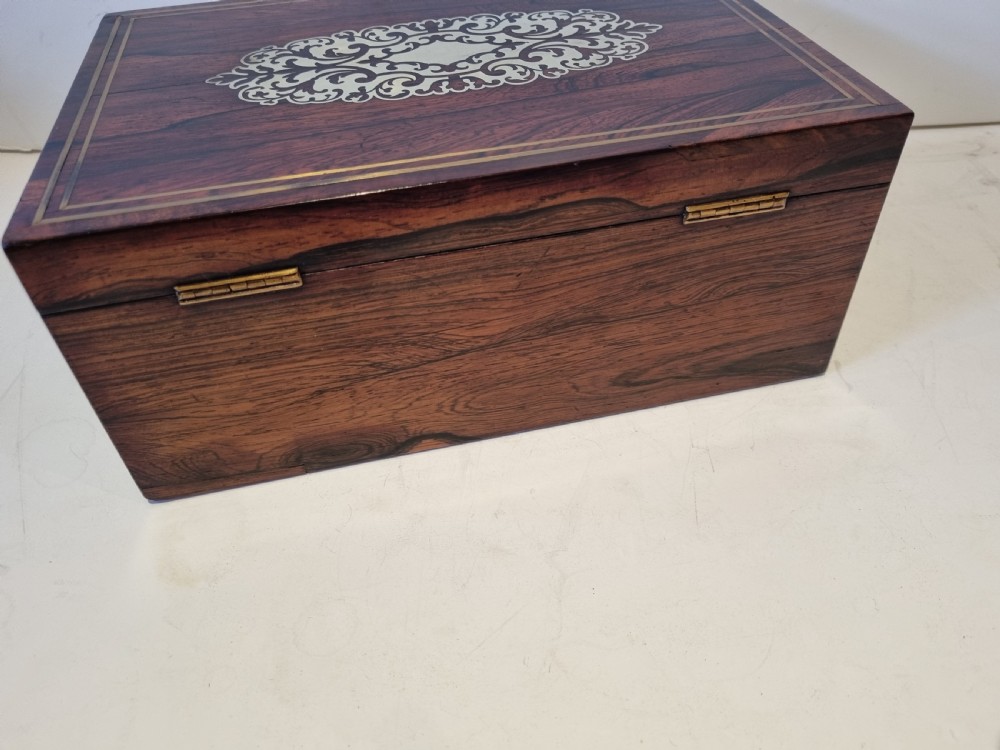 A rectangular dark rosewood box featuring intricate brass floral scrollwork inlay and brass double-stringing on the lid and front panel. View V