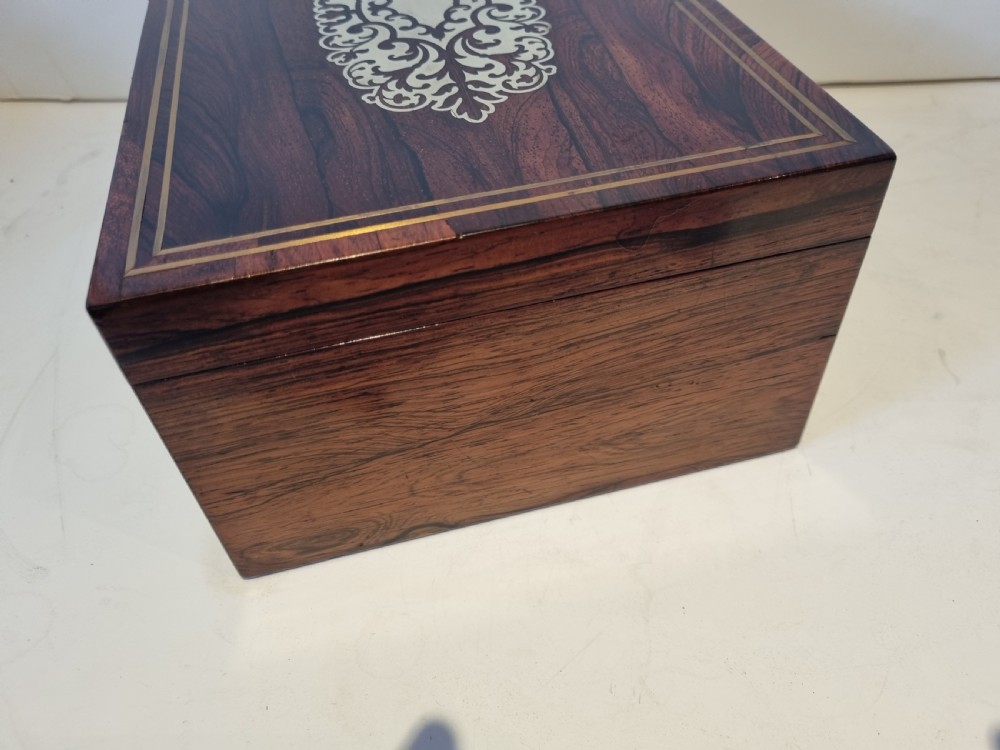 A rectangular dark rosewood box featuring intricate brass floral scrollwork inlay and brass double-stringing on the lid and front panel. View VI