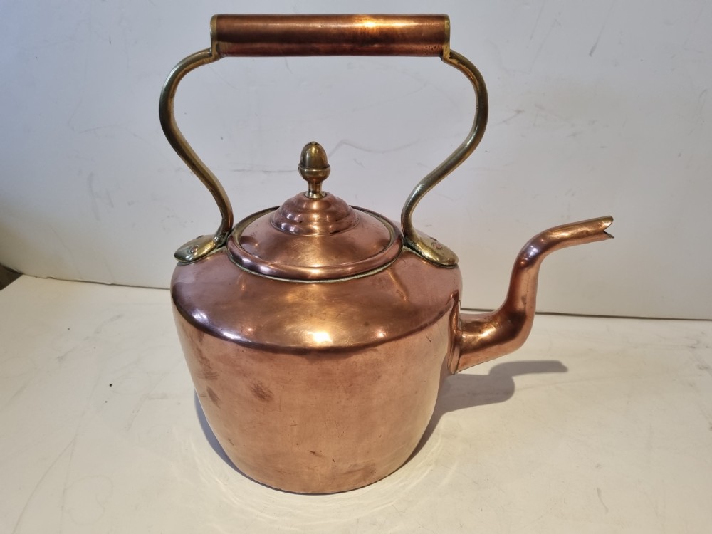 An antique Georgian copper tea kettle featuring a polished body, curved gooseneck spout, domed lid with an acorn finial, and an overhead brass handle.