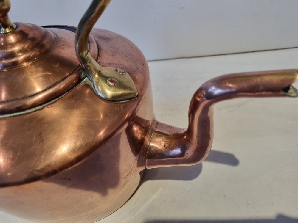 An antique Georgian copper tea kettle featuring a polished body, curved gooseneck spout, domed lid with an acorn finial, and an overhead brass handle. View VI
