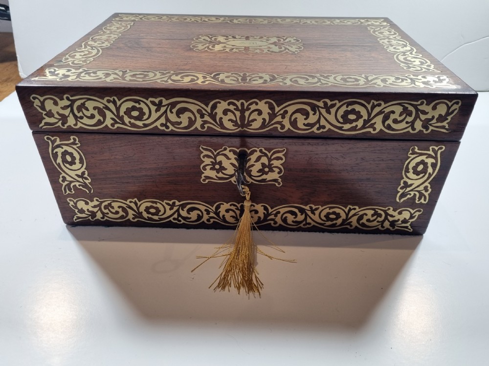A rectangular dark rosewood writing box featuring intricate brass floral scrollwork inlay around the borders and escutcheon, complete with a key and tassel.