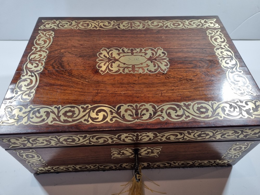 A rectangular dark rosewood writing box featuring intricate brass floral scrollwork inlay around the borders and escutcheon, complete with a key and tassel. View II