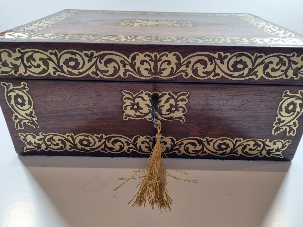 A rectangular dark rosewood writing box featuring intricate brass floral scrollwork inlay around the borders and escutcheon, complete with a key and tassel. View III