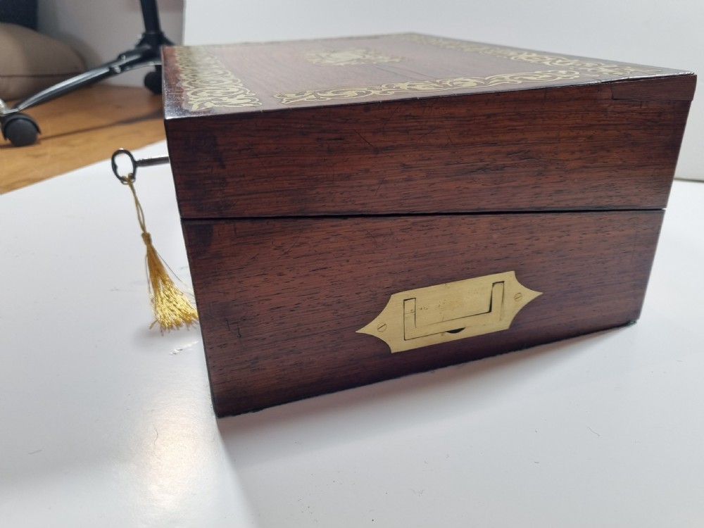 A rectangular dark rosewood writing box featuring intricate brass floral scrollwork inlay around the borders and escutcheon, complete with a key and tassel. View IV